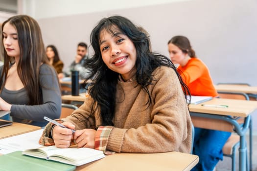 Young woman attending a university class, smiling and taking notes, surrounded by other students