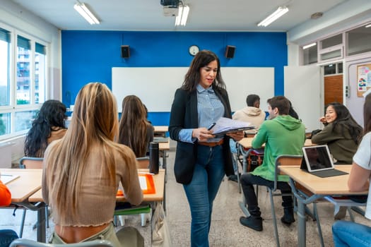 University or institute teacher holding documents walking through classroom during lesson with teen students sitting at desks