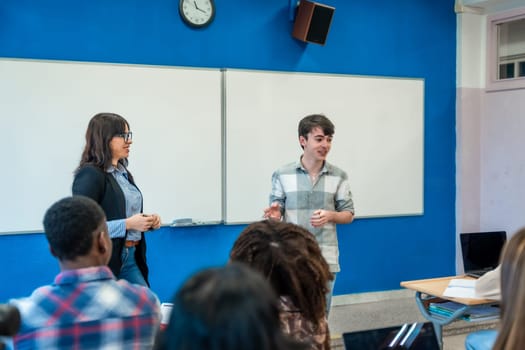 Teenage student giving a presentation in a modern classroom with a teacher and diverse group of students watching