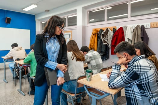 University teacher supervising students as they write exams in a classroom setting, fostering a focused and academic environment