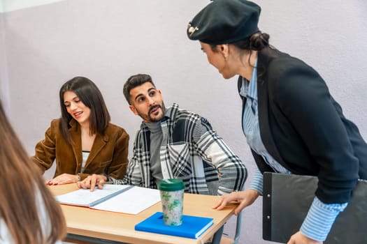 University students collaborating at a desk, engaging in study sessions while receiving guidance from their professor in a dynamic classroom setting