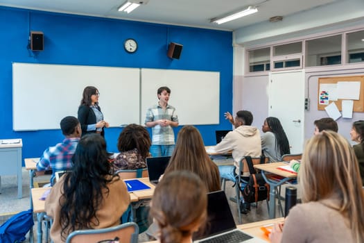 Male high school student giving a presentation in front of his diverse classmates and teacher in a modern classroom