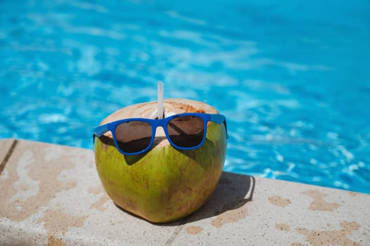 drinking coconut with a straw in sunglasses relax by the swimming pool at the resort in the hotel in the summer