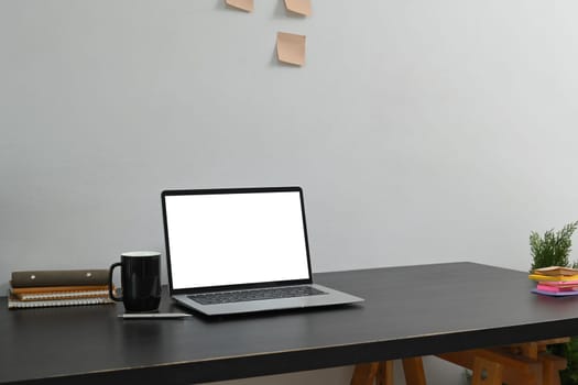 Laptop with a blank screen, a coffee mug, and stationery on black wooden desk.