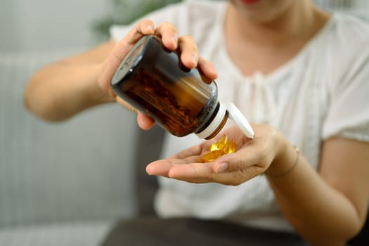 Middle aged woman pouring fish oil supplements from a brown bottle into her hand.