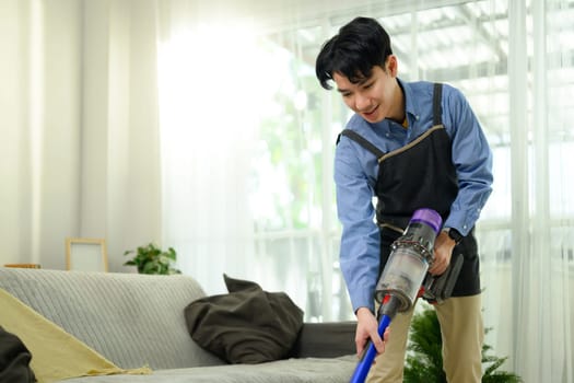 Smiling man vacuuming carpet in living room at home. Home care concept.