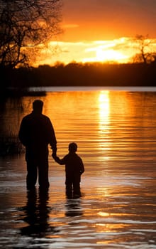 Father and son standing in water holding hands watching a beautiful sunset, creating silhouettes and reflections