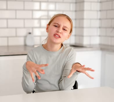 Cute Little Girl Sitting In The Kitchen At Home Showing Negative Emotions