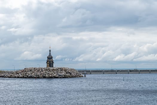 St. Petersburg, Russia - 08.07.24. The Chapel of St. Peter among the waves of the Gulf of Finland. A secluded shrine on a rocky embankment under a cloudy sky.