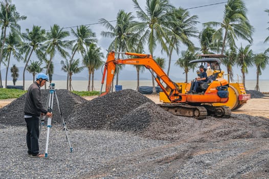 Construction heavy machinery excavator and builder with theodolite at a construction site on beach by sea in Asia. Nha Trang, Vietnam - December 14, 2024
