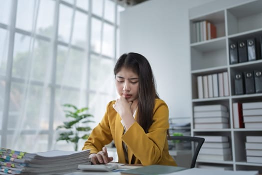 Thoughtful businesswoman analyzing data and documents in a modern office environment with natural light pouring in.