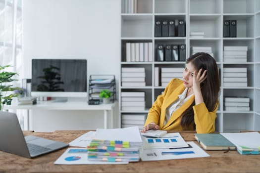 Young businesswoman in yellow blazer looking thoughtfully at documents while working in modern office space.