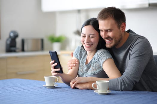 Happy interracial couple in love checking phone in the kitchen at home