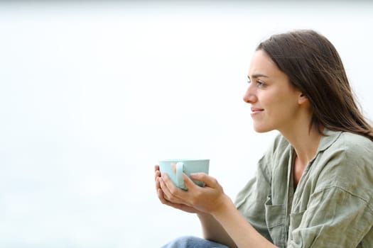 Profile of a relaxed woman on the beach drinking coffee