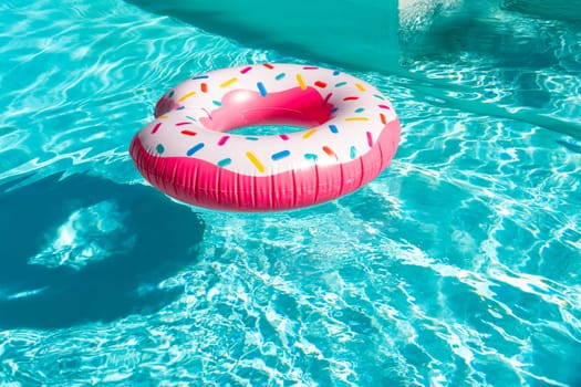 Pink donut-shaped inflatable float in turquoise swimming pool with shadow and sunlight reflections