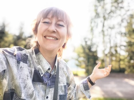 A middle-aged woman smiles as she takes a selfie in a beautiful natural landscape, capturing her travel adventure.