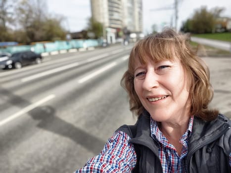 A middle-aged blonde woman captures a cheerful selfie on a lively city street while exploring.