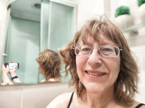 Blonde woman captures a cheerful morning selfie in her bathroom mirror while getting ready for the day.