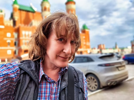 Female traveler blogger takes a cheerful selfie in a bustling city while enjoying her summer trip adventure.