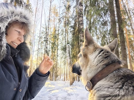 Blonde woman smiling while taking a selfie with her German Shepherd dog during a winter excursion in the woods.
