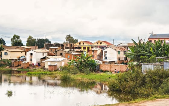 Antananarivo, Madagascar - April 24, 2019: Group of unknown Malagasy children standing in front of their house, grass and flooded rice fields foreground, typical scenery in suburbs of Antananarivo