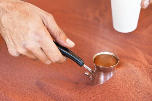 Coffee prepared on street in traditional Arabic way, cezve or ibrik (small Turkish coffe pot) is placed in red hot sand until liquid boils