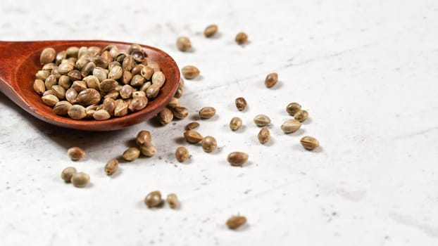 Unpeeled hemp - Cannabis sativa - in small dark wooden spoon on white stone board desk