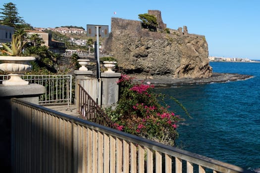 Stunning view of Catania rocky cliffs, a medieval fortress, and vibrant sea, framed by a decorative urn with a succulent, perfect for scenic landscapes.