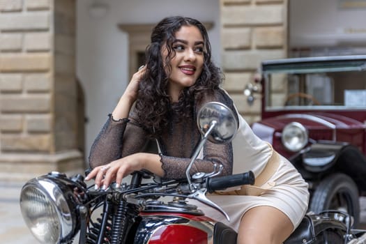 Attractive young woman with long black hair is sitting in a sexy pose on  vintage motorcycle. Horizontally.