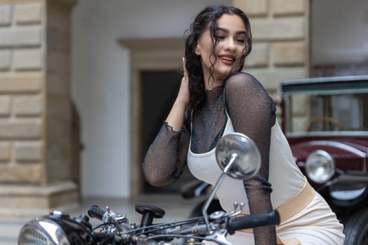 Beautiful long hair young woman is posing on the vintage motorcycle.  Horizontally.