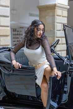 Attractive young woman is getting out of the vintage car. Vertically.
