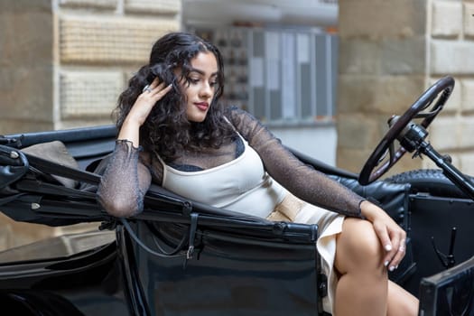 Cool long black hair tanned girl is resting in a vintage open car. Horizontally.