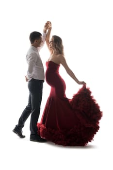 Side view of elegant man dancing with pregnant woman in red maxi dress on white background in studio