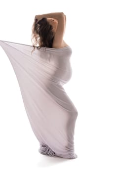Naked serene pregnant female wrapped in cloth walking with closed eyes on white background in studio
