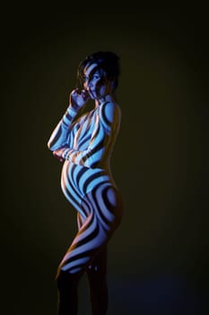 Side view of sensual nude pregnant female in dark studio with stripes shadows body paint