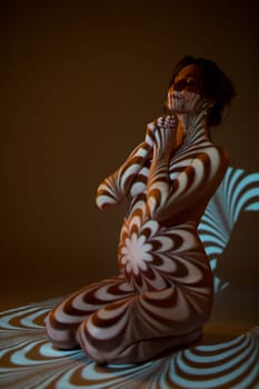 Side view of naked pregnant female sitting with closed eyes on floor in dark studio with ornamental projector shadows on body