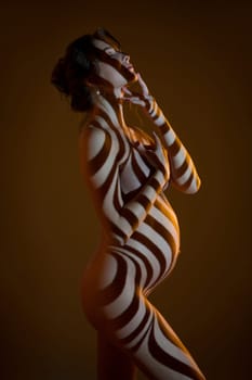 Side view of sensual nude pregnant female in dark studio with stripes shadows on body from projector