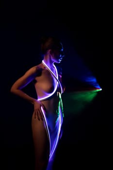Seductive young slim nude female with glowing blue neon wire wrapped around body touching face while standing with eyes closed in dark studio