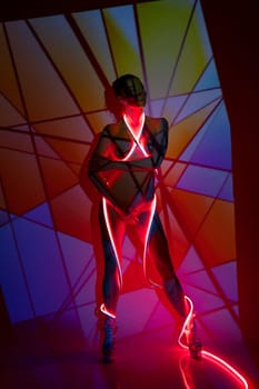 Artwork portrait of naked slim female model with bright neon strap standing under colorful projector illumination forming pattern on body and wall