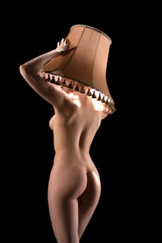 Slim curvy naked female model covering head and face with beige lampshade back view