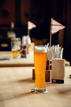 A tall glass of cold wheat beer with a frothy head on a wooden table in a cozy pub. A perfect scene for beer enthusiasts, Oktoberfest, and hospitality-themed visuals