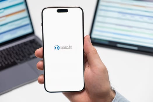 PRAGUE, CZECH REPUBLIC - JANUARY 21 2024: Diners Club International logo on the screen of smartphone in mans hand on the workplace background.