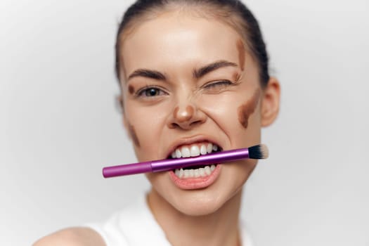 A young model demonstrates confidence and fun while applying makeup with a brush, featuring joyful expression and artistic elegance in a clean white background.