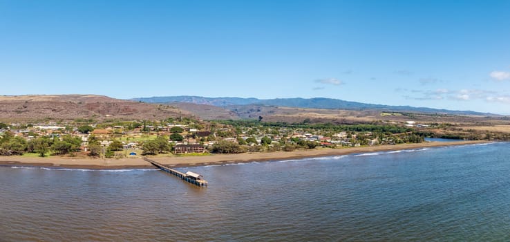 Panoramic aerial shot showing serene beauty of Waimea, Kauai showcasing its pier, coastline, and the landscape beyond under a clear sky
