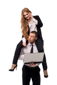 Businesswoman in formal wear speaking on smartphone while sitting on shoulders of businessman using laptop isolated on white background