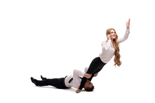Full length of male manager lying on floor and supporting legs female colleague talking smartphone and reaching hand up representing concept of business relationship