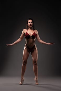 Strong brunette in red bra and panties ready for figure and fitness competition looking at camera against gray background