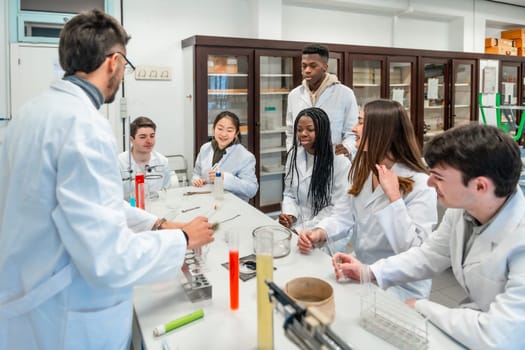 Multi ethnic university students wearing lab coats listening to their chemistry teacher explaining a scientific experiment in a school laboratory