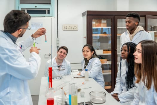 Multi ethnic group of university students attending a chemistry lesson in a laboratory, teacher showing a test tube with a chemical reaction