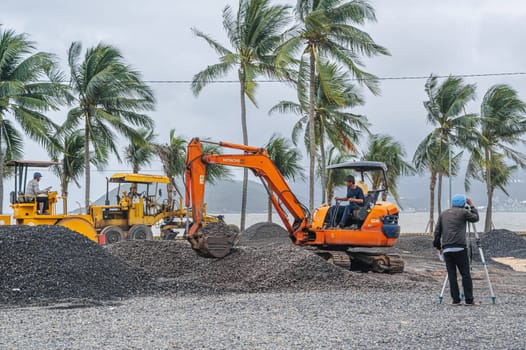 Construction heavy machinery excavator and builder with theodolite at construction site on a beach by sea in Asia. Nha Trang, Vietnam - December 14, 2024
